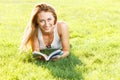 Close up portrait of an attractive young woman laying down on green grass in a park during the summer and listening to Royalty Free Stock Photo