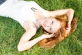 Close up portrait of an attractive young woman laying down on green grass in a park during the summer and listening to Royalty Free Stock Photo