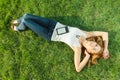 Close up portrait of an attractive young woman laying down on green grass in a park during the summer and listening to Royalty Free Stock Photo