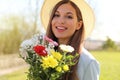 Close up portrait of an attractive young woman in straw hat holding flower bouquet and looking at camera standing outdoor Royalty Free Stock Photo