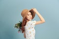 Close up portrait of an attractive young woman in summer dress and straw hat holding flower bouquet and looking over her shoulder Royalty Free Stock Photo