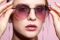 Close-up portrait of attractive young woman in tinted glasses on pink background Royalty Free Stock Photo