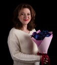 Close-up portrait of an attractive young woman in a white sweater holding a bouquet of roses and orchids on a black background Royalty Free Stock Photo