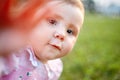 Close-up portrait of the baby girl against green meadow looking up to camera outdoors in sunlight. Royalty Free Stock Photo