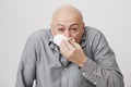 Close-up portrait of bald man sneezing and wiping nose with napkin or tissue while having allergy or runny nose Royalty Free Stock Photo