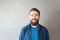 portrait of bearded biracial handsome young man with eyebrow piercing smiling against grey wall Royalty Free Stock Photo