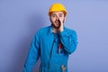 Close up portrait of bearded handsome male constructor yelling something and keeping hands near his opened mouth, foreman wearing