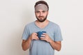 Close up portrait of bearded man in dressing gown and mask to sleep on his head, holding blue mug in his hands, looking directly Royalty Free Stock Photo