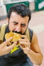Close up portrait of bearded man eating burger. Portrait of expressive fat man eating hamburger with meat, tomato, bacon, onion