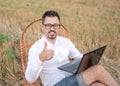 Close up portrait of bearded man with laptop sitting in a rocking chair outdoors. Happy caucasian man showing thumb up