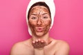 Close up portrait of beatiful European female blowing kiss, putting chocolate face mask, being naked, covering her hair with white Royalty Free Stock Photo