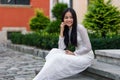 Close up portrait of beautiful asian girl dressed in Ao Dai white dress sitting on the stairs in courtyard. Royalty Free Stock Photo