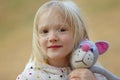 Close-up portrait of beautiful blond toddler girl hugging her favorite handmade toy knitted cat outdoors. Royalty Free Stock Photo