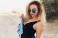Close-up portrait of beautiful blonde model in black swimsuit and sunglasses posing on the beach. A girl with a Royalty Free Stock Photo