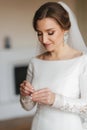 Close up portrait of beautiful bride standing by the window at home and tying on earrings. Charming bride in white Royalty Free Stock Photo