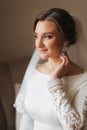 Close up portrait of beautiful bride standing by the window at home and tying on earrings. Charming bride in white Royalty Free Stock Photo