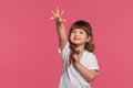 Close-up portrait of a little brunette girl dressed in a white t-shirt posing against a pink studio background. Sincere Royalty Free Stock Photo