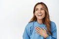 Close up portrait of beautiful brunette woman laughing, smiling and holding hand on chest, chuckle carefree, skin care