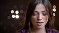 Close-up portrait of beautiful caucasian brunette girl watching downwards with contempt on blurred lights background.