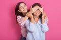 Close up portrait of beautiful Caucasian woman covering eyes to her friend standing behind and smiling, looking at girl wears blue Royalty Free Stock Photo