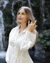 Close up portrait of beautiful Caucasian woman near waterfall. Female with long blond hair wearing white dress. Water splash. Royalty Free Stock Photo