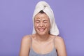 Close up portrait of beautiful Caucasian young woman with white towel on her head puts scrub or mask on her face while taking care