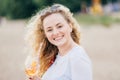 Close up portrait of beautiful European female with light wavy hair, toothy smile, holds cold fresh beverage, enjoys sunny good we