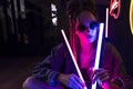 Close up portrait of a beautiful girl with an cornrows, wearing a denim jacket and sunglasses, holds in her hands neon night club