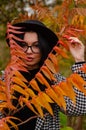 Close up portrait of a Beautiful girl in a dark dress and black hat standing near colorful autumn leaves. Art work of Royalty Free Stock Photo