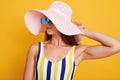 Close up portrait of beautiful girl wearing striped colored swimming suit, hat and sun glasses, adorable female tounching her cap Royalty Free Stock Photo