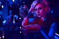 Close up portrait of beautiful glam blond woman sitting at the bar in the night club in colourful neon lights drinking cocktail Royalty Free Stock Photo