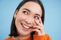 Close up portrait of beautiful japanese woman, smiling and laughing, touches her face, standing over blue studio Royalty Free Stock Photo