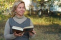 Attractive mature woman reading a book in the park. Moment of leisure. Outdoor relax. Space for text. Royalty Free Stock Photo