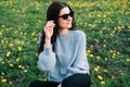 Close up portrait of beautiful millennial young woman in sunglasses sitting on meadow with yellow chamomile flowers and grass in Royalty Free Stock Photo