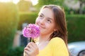 Close-up portrait of beautiful preteen girl holding purple allium onion flower in garden outdoors at sunset looking up daydreaming Royalty Free Stock Photo