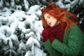 Close up portrait of a beautiful red-haired girl leaning on snowy fir tree bough with dreaming look. Royalty Free Stock Photo
