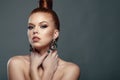 Close up portrait of beautiful red-haired model with her hair scraped back into a high bun holding her hands at her neck