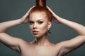 Close up portrait of beautiful red-haired model with her hair scraped back into a high bun holding her hands up touching it