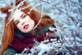 Close up portrait of a beautiful red-haired young woman looking into the camera through icy and snowy branches. Royalty Free Stock Photo