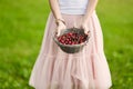 Portrait of a beautiful romantic brunette girl with a basket of cherries in a green garden