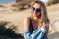 Close-up portrait of beautiful smileing blonde model in black swimsuit and sunglasses posing on the beach. A girl with a Royalty Free Stock Photo