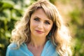 Close-up portrait of beautiful smiling blonde 40 years old woman in blue shirt looking in camera outdoors in back light. Healthy Royalty Free Stock Photo