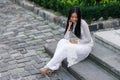 Close up portrait of beautiful asian girl dressed in Ao Dai white dress sitting on the stairs in courtyard. Royalty Free Stock Photo