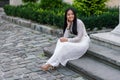 Close up portrait of beautiful asian girl dressed in Ao Dai white dress sitting on the stairs in courtyard. Royalty Free Stock Photo