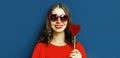 Close up portrait of beautiful smiling young woman with lollipop wearing a red heart shaped sunglasses over a blue Royalty Free Stock Photo