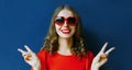 Close up portrait of beautiful smiling young woman wearing a red heart shaped sunglasses over a blue Royalty Free Stock Photo