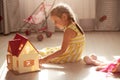 Close up portrait of beautiful toddler girl with pigtails sitting on floor playing with toy doll house, toy baby carriage near Royalty Free Stock Photo