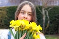 Close up portrait of beautiful tween romantic girl holding bouquet of bright yellow spring daffodil flowers at her face hugging it