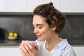 Close up portrait of beautiful woman, drinking coffee at home, looking tender and relaxed, enjoys weekends indoors