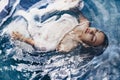 Close up portrait of beautiful woman lying in water with fabric. Royalty Free Stock Photo